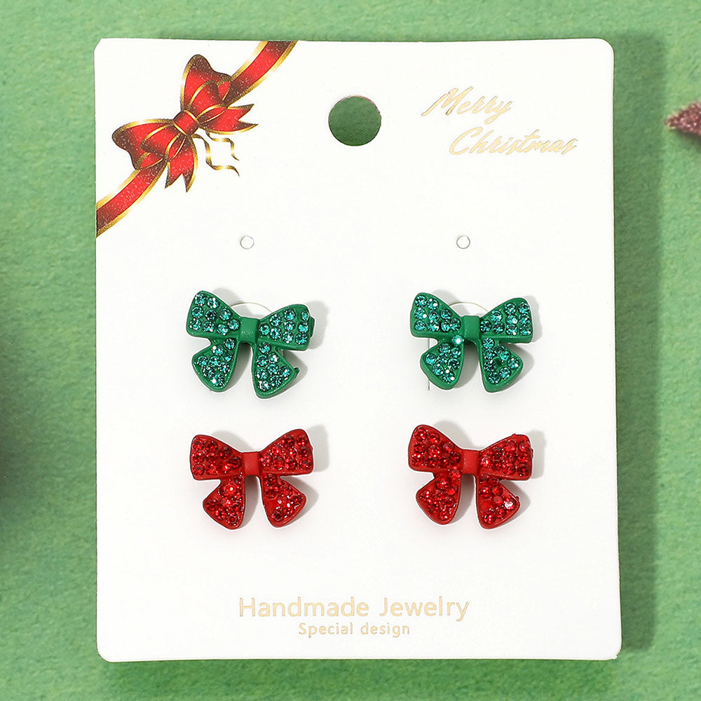 The image features a holiday-themed earring set showcasing two pairs of bow-shaped stud earrings. One pair is adorned with sparkling green rhinestones, while the other pair features bright red rhinestones.
