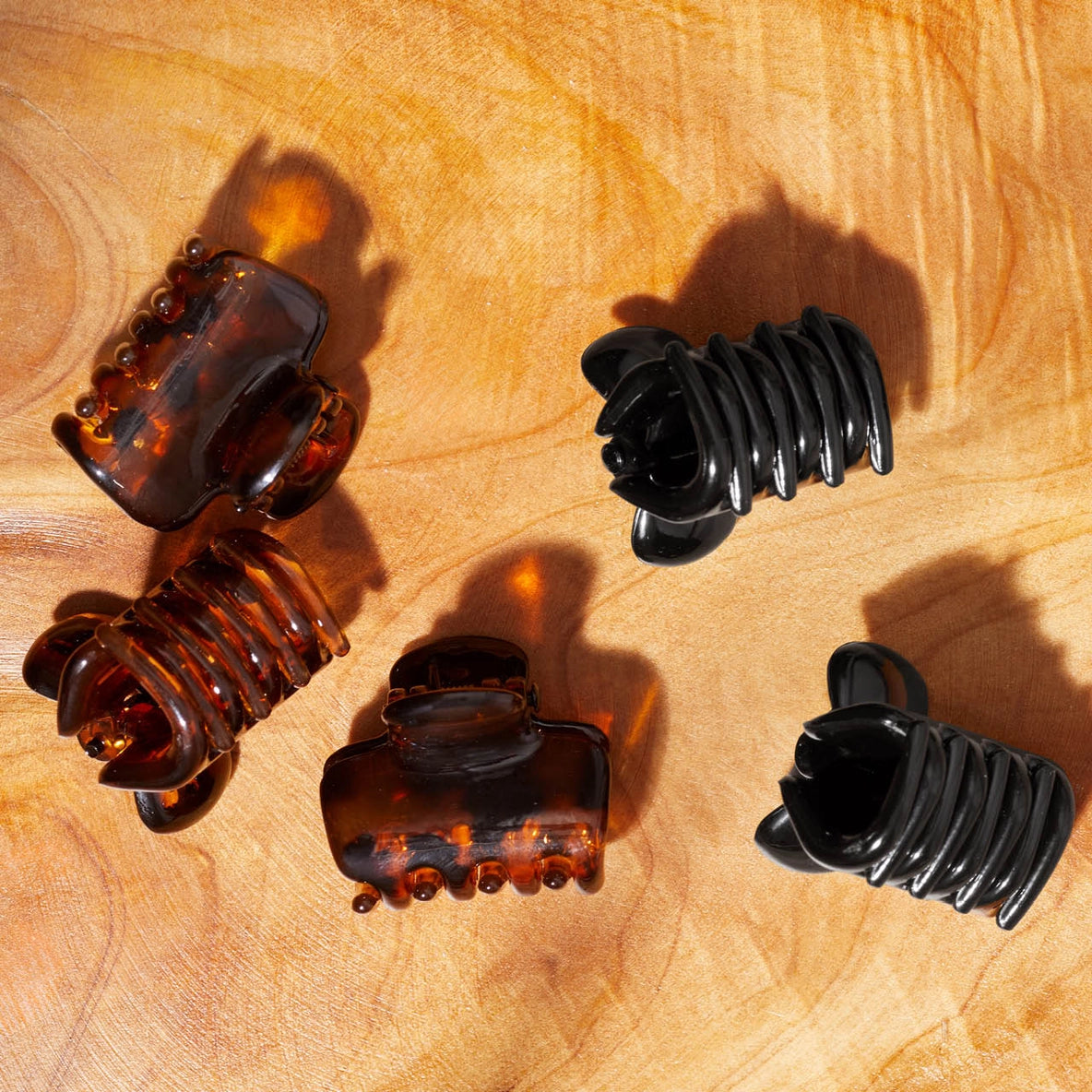 A set of six hair claw clips is displayed on a wooden surface, featuring three glossy black clips and three tortoise shell clips. The clips are designed with a puffy shape, showcasing their eco-friendly construction from recycled plastic.