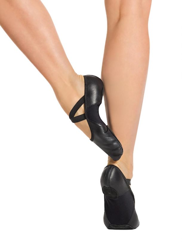 A dancer is facing away from the camera, wearing black Leather Hanami ballet shoes without tights on, showcasing the split sole and elastic criss-cross straps. The shoes are positioned on a white background, highlighting their sleek design and flexibility.