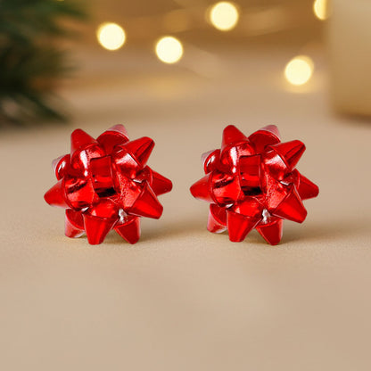 A pair of vibrant red holiday gift bow stud earrings is displayed against a soft, neutral background. The earrings feature a playful, dimensional bow design with glossy finishes, capturing festive charm perfect for holiday.