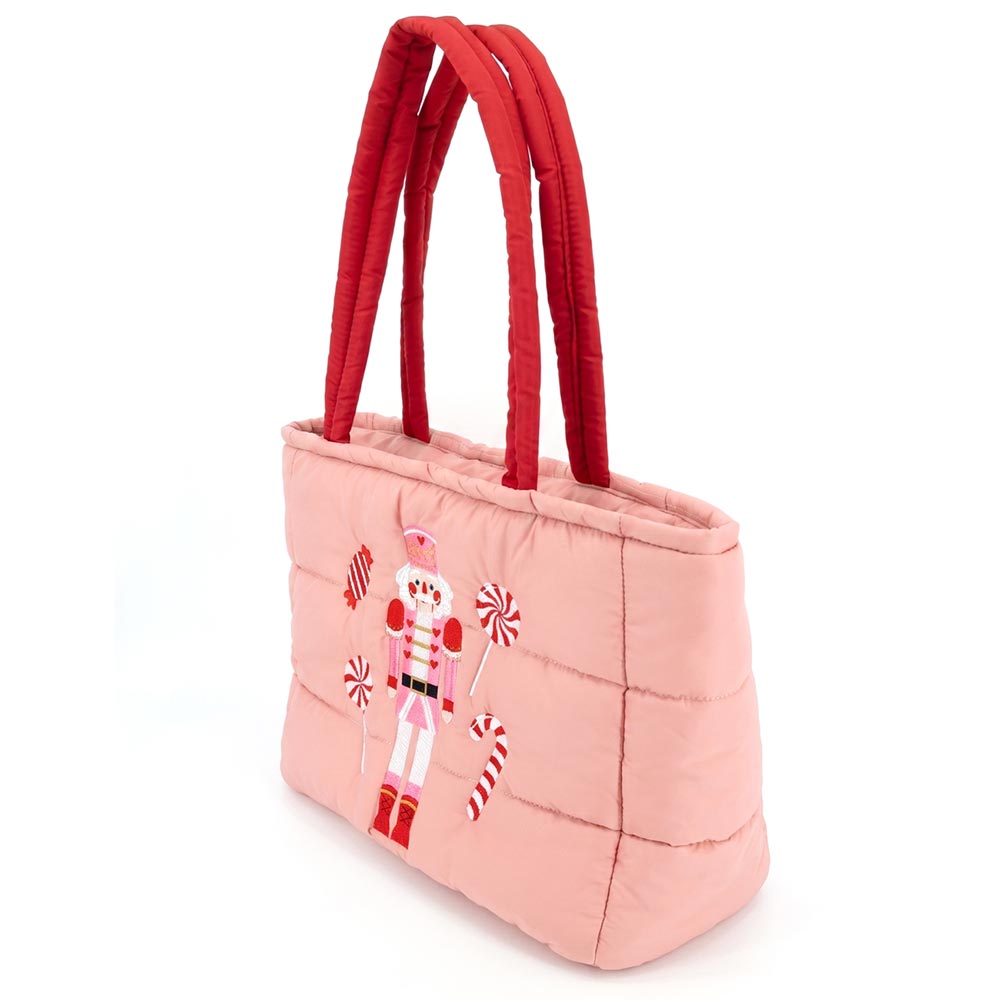 A pink quilted tote bag features an embroidered nutcracker design alongside candy canes, showcasing a festive holiday theme.
