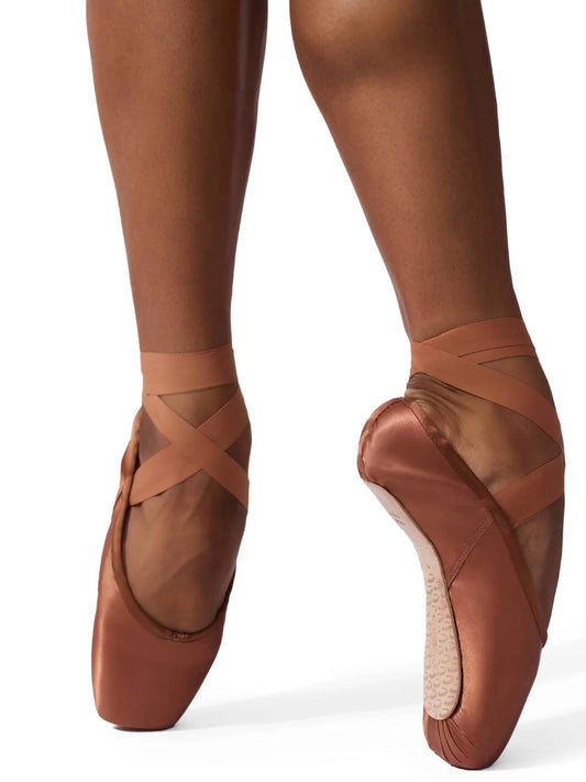 Ava 1142W pointe shoe in a warm maple color, featuring a satin finish and elastic drawstrings. The shoe is worn on a dancers foot, showcasing its broad toe box and crossed ribbons.