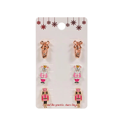 The image features a Nutcracker Trio Earring Set by an unspecified brand, displayed on a card. The set includes three pairs of holiday-themed stud earrings: a pair of ballet slippers in rose gold, a pair depicting a pink-dressed.