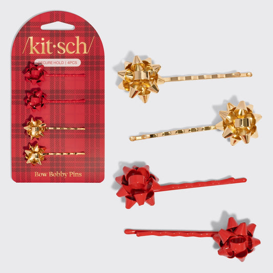 A set of four bobby pins featuring festive gift bow designs in red and gold is displayed alongside its packaging.