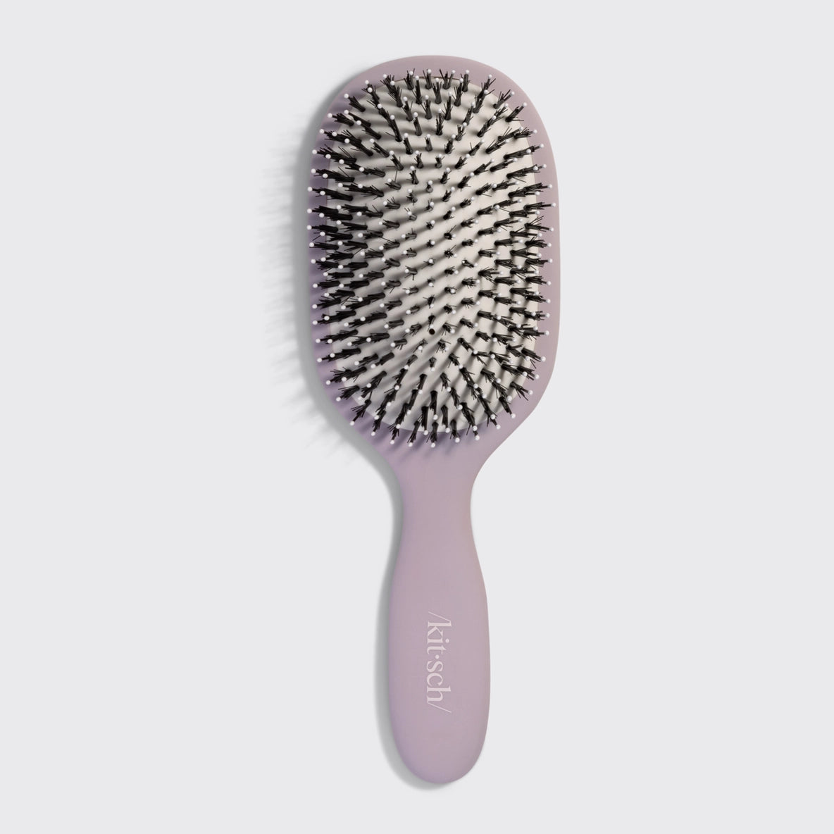 The image showcases a Kitsch Smooth & Polish Brush in a soft lavender color. The brush features a wide paddle design with a mix of vegan boar and nylon bristles, ideal for smoothing and detangling hair while ensuring comfort during use.