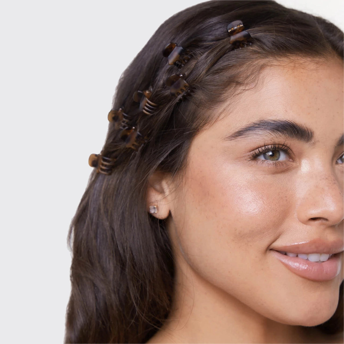 A model showcases the Kitsch Recycled Plastic Micro Classic Claw Clips in tortoiseshell, with several clips adorning her dark, wavy hair.