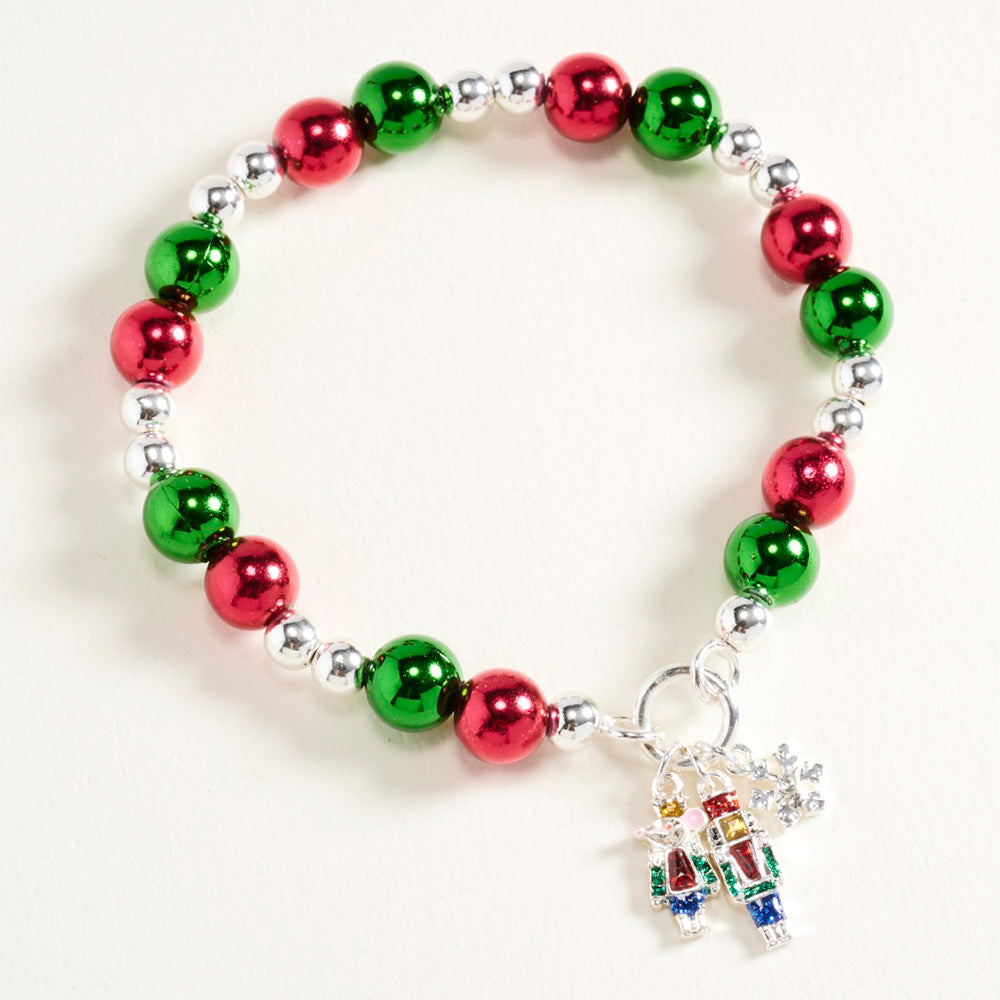 A festive Nutcracker Snowflake Charm Beaded Stretch Bracelet features vibrant red and green beads interspersed with silver accents.