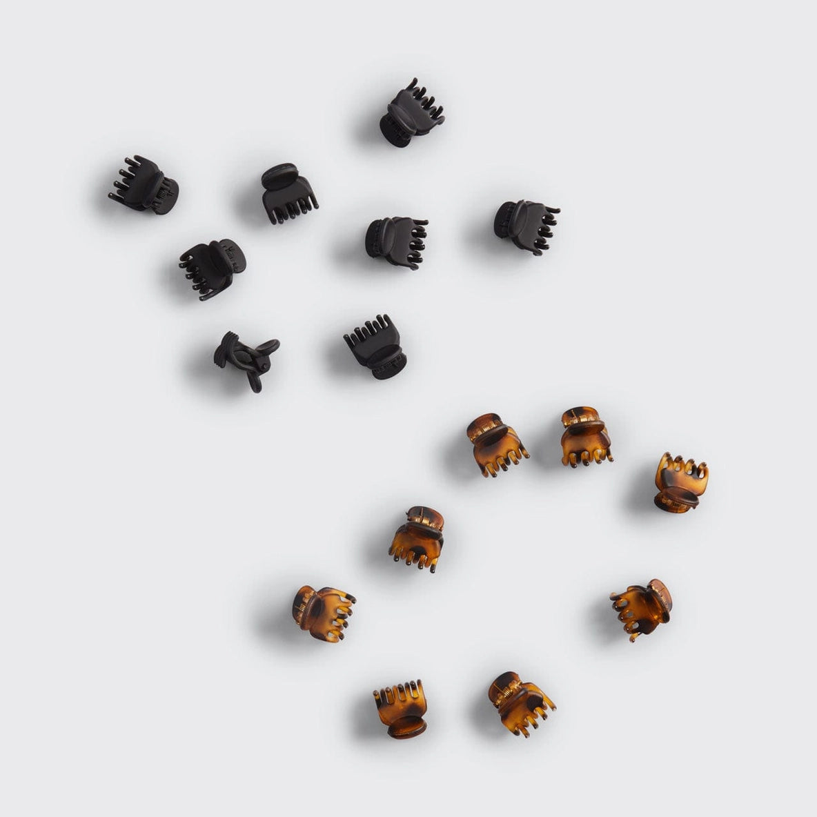A collection of 16 mini claw clips from Kitsch, featuring a mix of black and tortoiseshell designs. The clips are scattered against a light gray background, showcasing their stylish and eco-friendly design made from recycled.