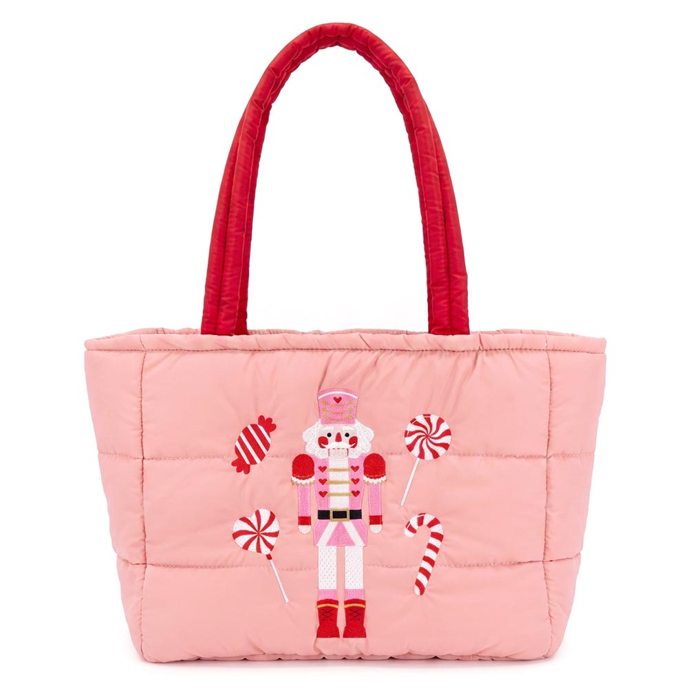 A festive pink quilted tote bag features an embroidered nutcracker surrounded by candy cane designs. The bag has red shoulder handles and a spacious main compartment, perfect for carrying holiday essentials.