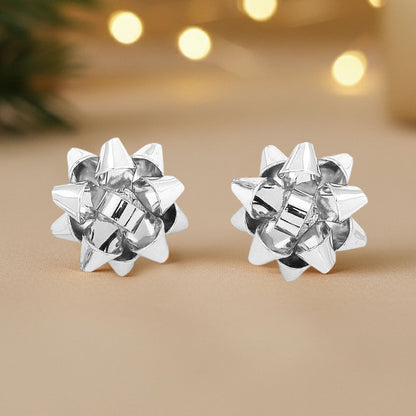 Silver holiday gift bow stud earrings are displayed on a soft, neutral background, showcasing their playful, dimensional design.