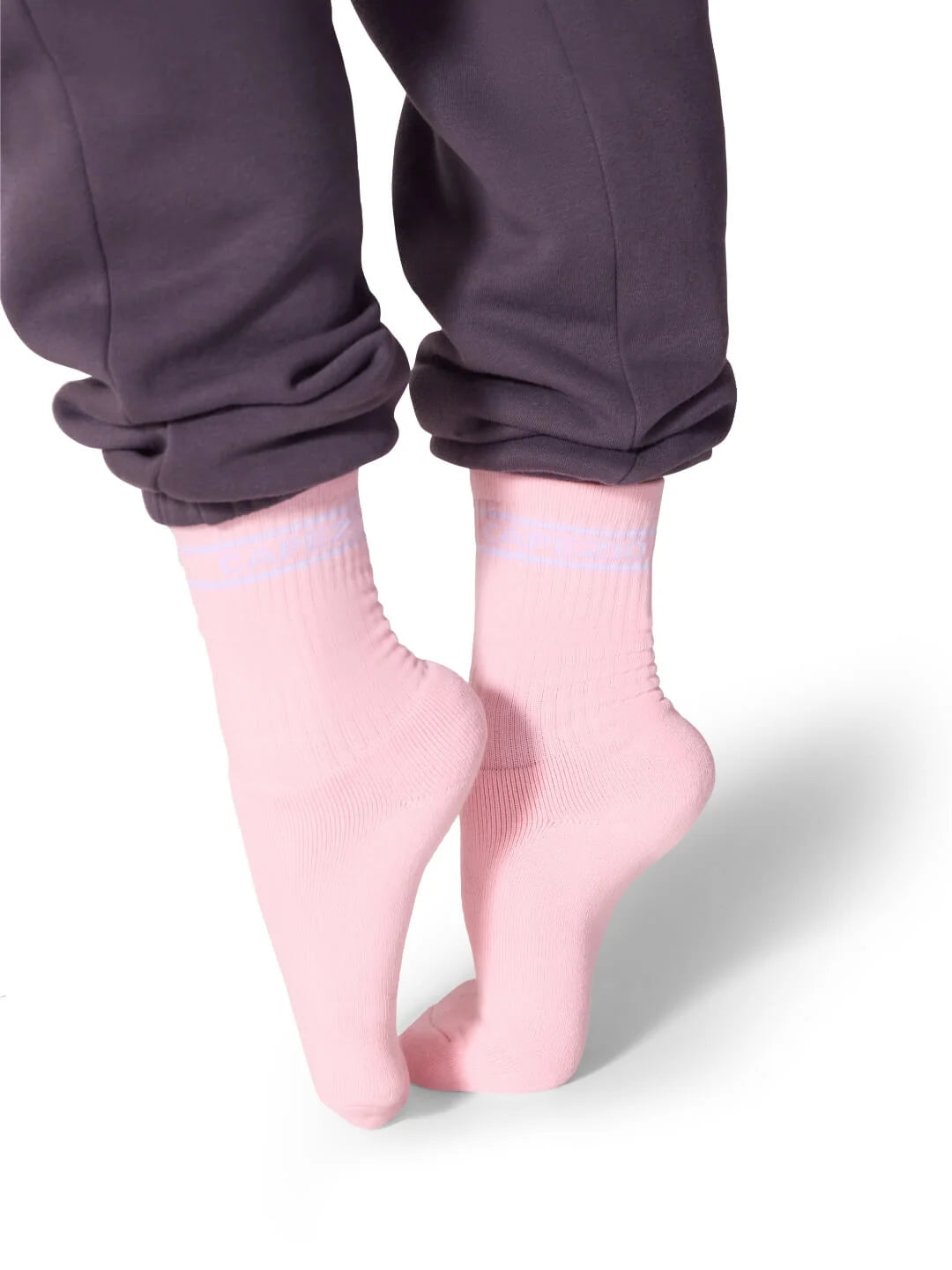 A person is wearing light pink Varsity Crew Socks from Capezio, visible just above the ankle, while standing on tiptoe.