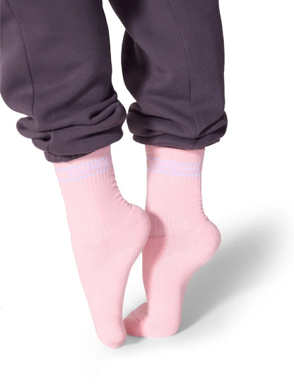 A person is wearing light pink Varsity Crew Socks from Capezio, visible just above the ankle, while standing on tiptoe.
