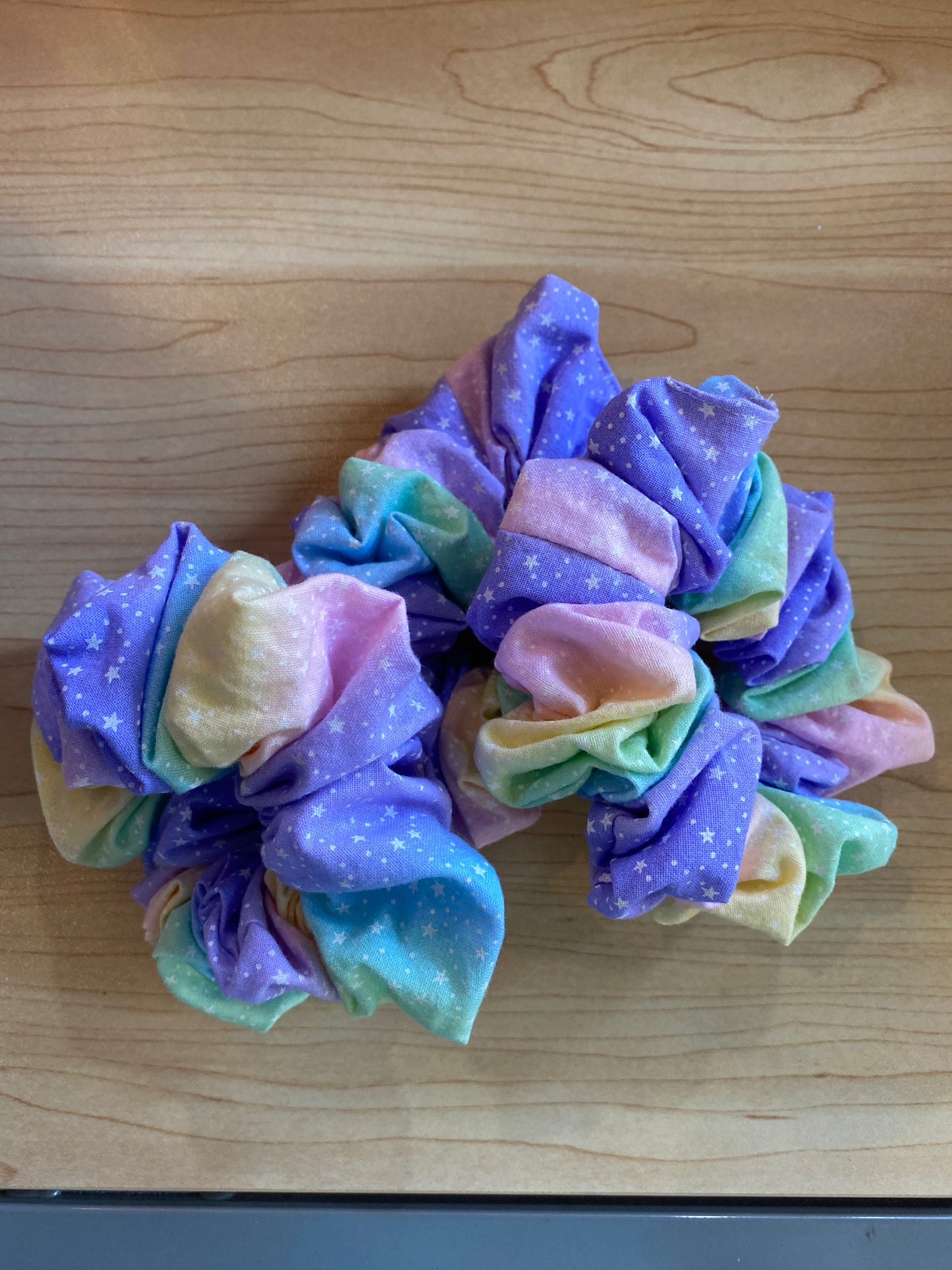 A set of three handmade scrunchies featuring a vibrant ballerina pattern in pastel colors, including purple, pink, and green, adorned with white star motifs.