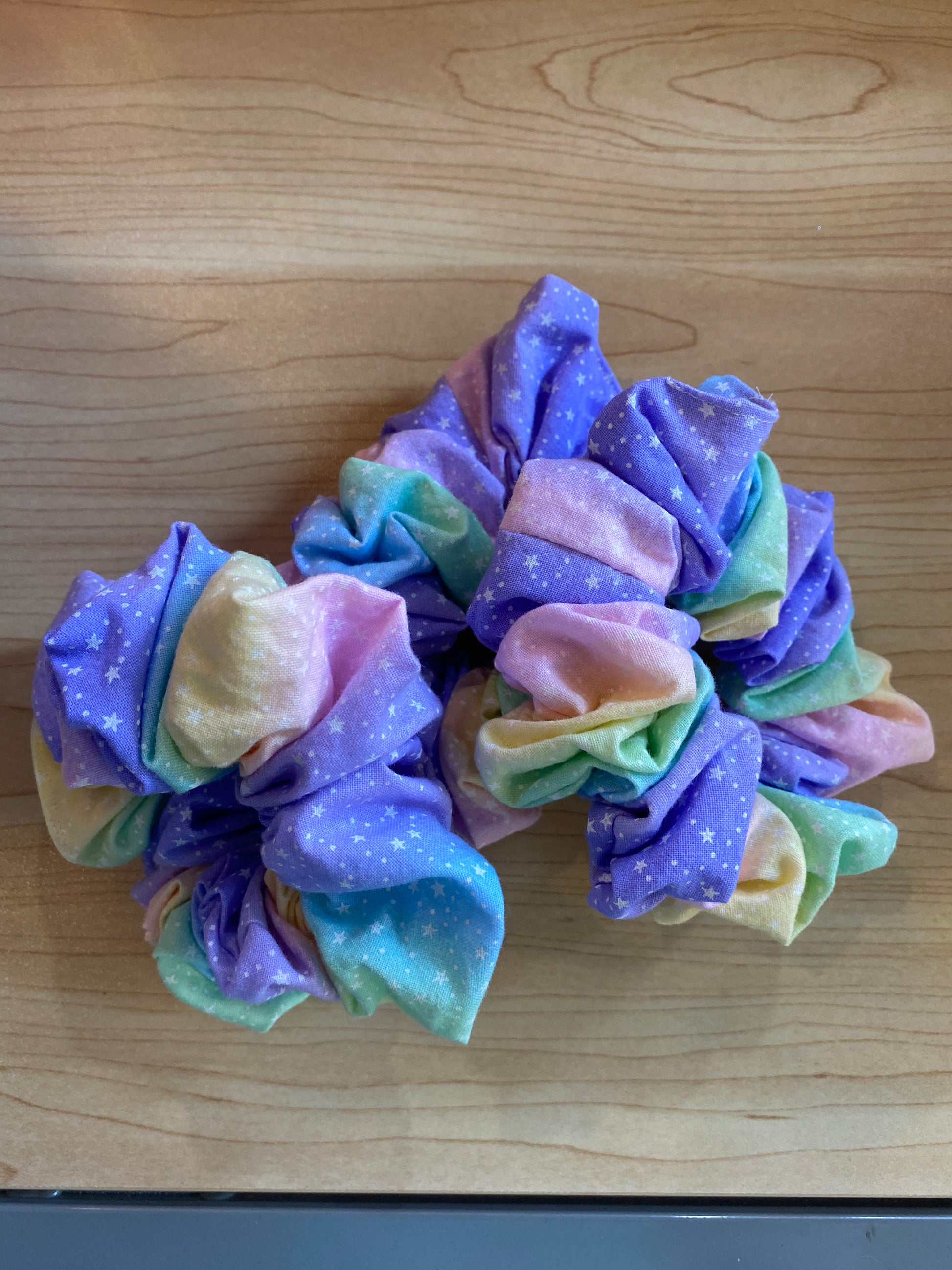 A set of three handmade scrunchies featuring a vibrant ballerina pattern in pastel colors, including purple, pink, and green, adorned with white star motifs.