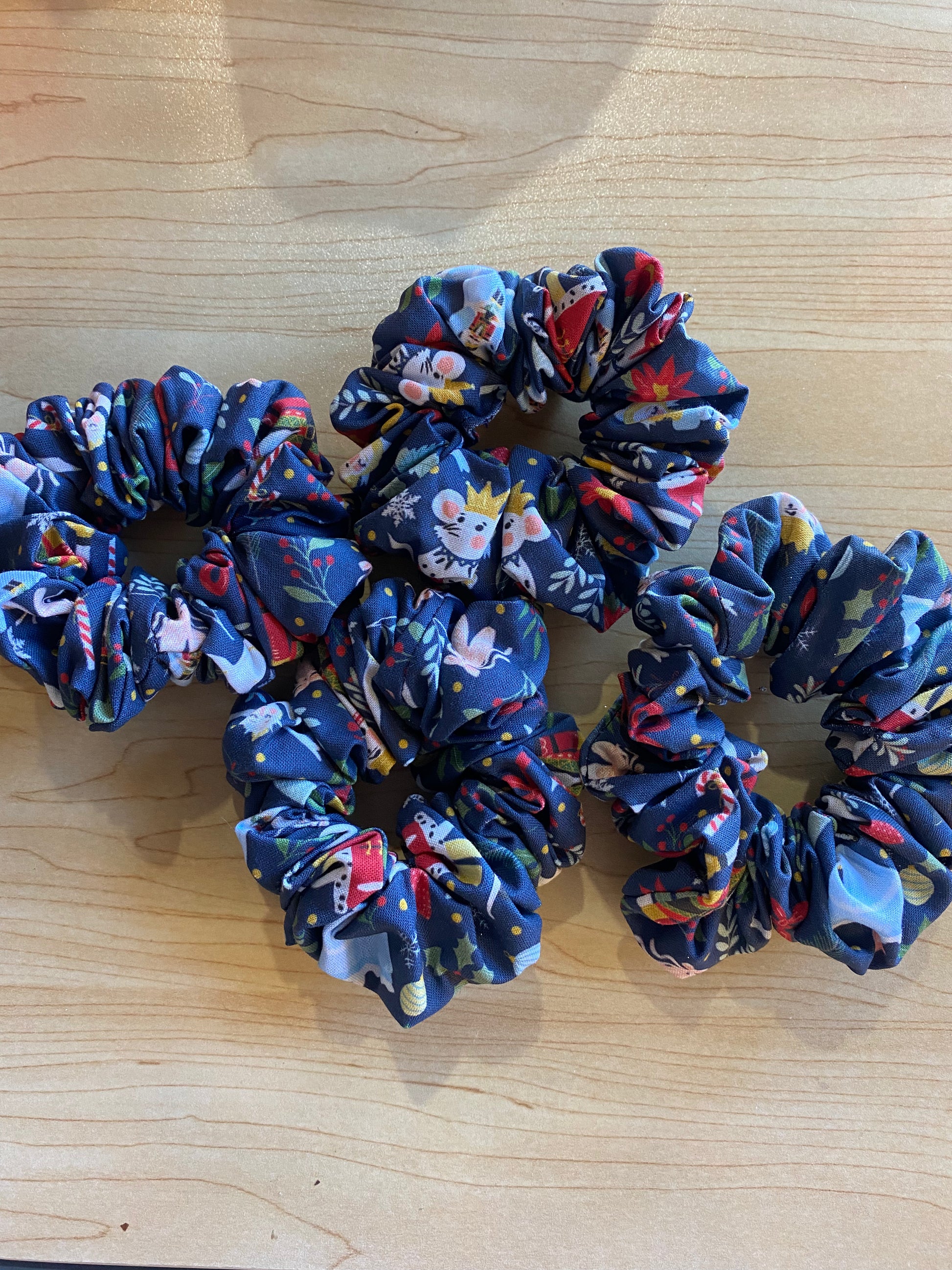 A collection of four handmade scrunchies featuring a vibrant ballerina pattern on a dark blue background. Each scrunchy is crafted from soft fabric, showcasing various floral and whimsical designs, making them stylish hair accessories.