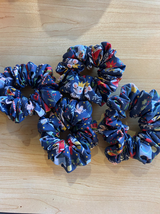 A collection of four handmade scrunchies featuring a vibrant ballerina pattern on a dark blue background. Each scrunchy is crafted from soft fabric, showcasing various floral and whimsical designs, making them stylish hair accessories.