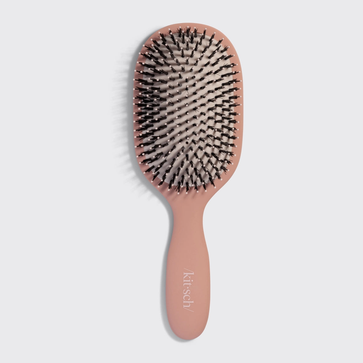 The image features a smooth and polished hairbrush by Krisch, showcasing a soft pink handle and a cushioned rubber pad.