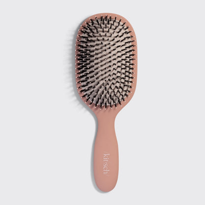 The image features a smooth and polished hairbrush by Krisch, showcasing a soft pink handle and a cushioned rubber pad.