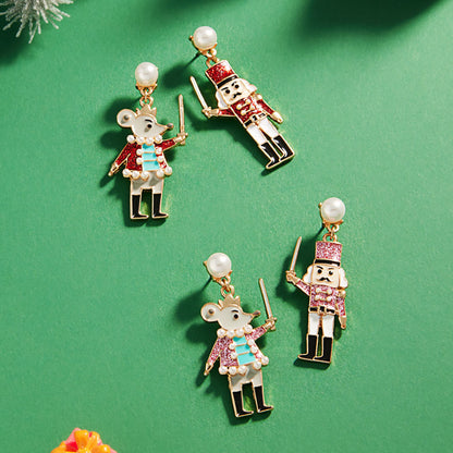 A festive pair of Enamel Nutcracker Dangle Earrings features whimsical designs of a nutcracker soldier and a mouse, each holding a sword.