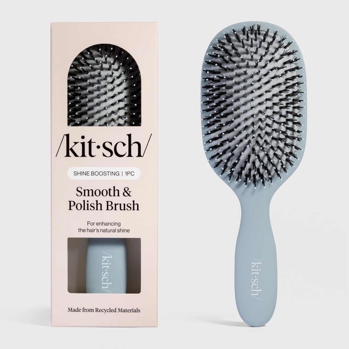 A light blue Kitsch Smooth & Polish Brush is displayed next to its packaging, featuring a clear window that showcases the brush inside.