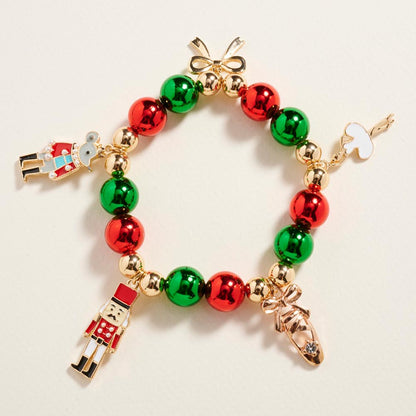 A festive Nutcracker Bow Charm Beaded Stretch Bracelet features alternating red and green beads, accented with gold elements.