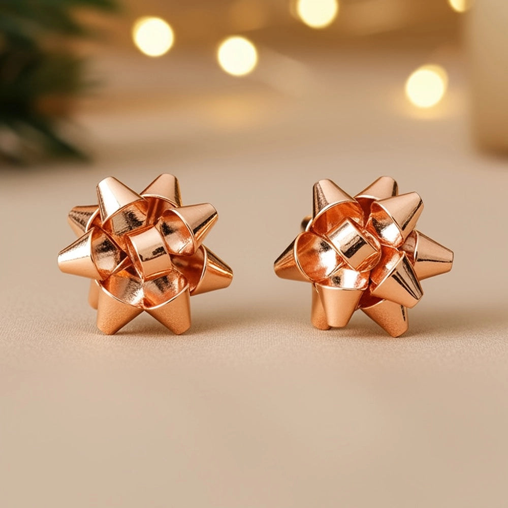 A pair of rose gold holiday gift bow stud earrings is displayed on a soft, neutral background. The earrings feature a playful, dimensional bow design, showcasing a shiny metallic finish that adds a festive charm, perfect for holiday.