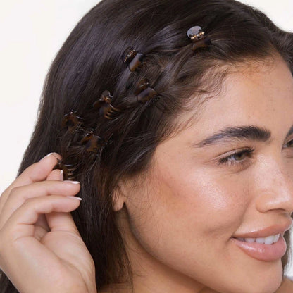 A woman with long, dark hair is smiling while showcasing multiple Kitsch Mini Claw Clips in a tortoiseshell pattern.