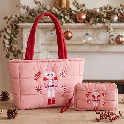 A festive pink quilted tote bag features an embroidered nutcracker and candy cane design, showcasing red handles and a spacious main compartment.
