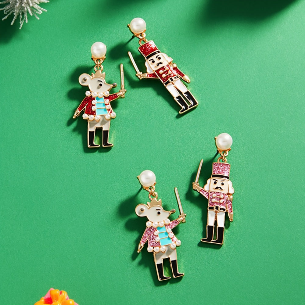 A pair of whimsical enamel nutcracker dangle earrings features a mouse and a nutcracker soldier, each adorned with colorful detailing.