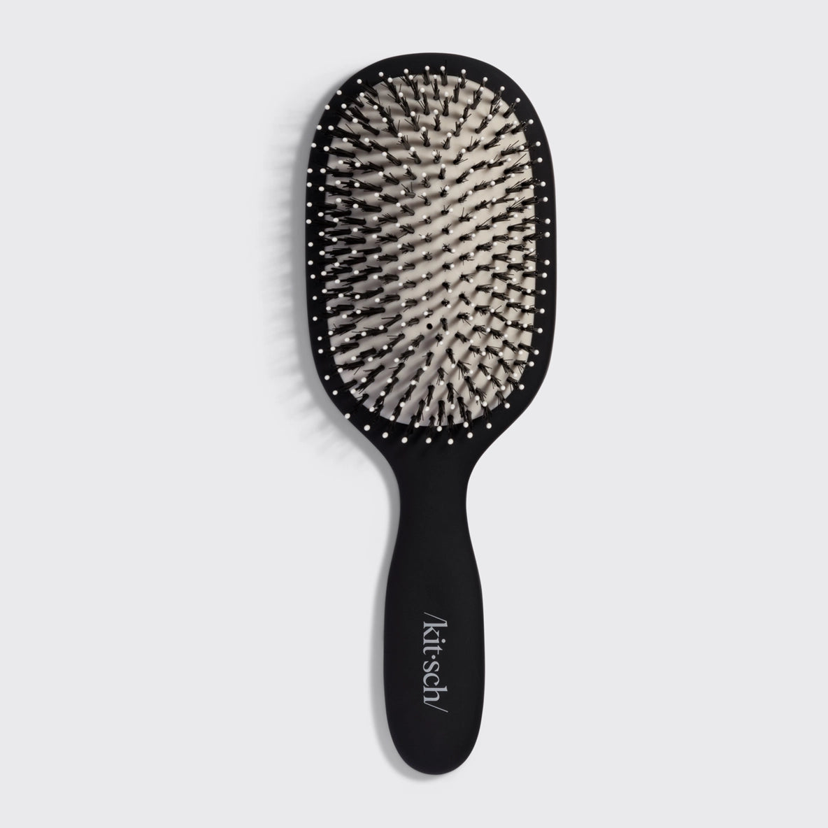 A black Smooth & Polish Brush by Kitsch features a wide paddle design with dual-bristle technology, combining vegan boar and nylon bristles for effective smoothing and detangling.