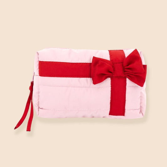 A pink quilted cosmetic pouch bag with a red bow and a red stripe across the front, designed to resemble a gift. It features a secure zipper closure and a compact size, ideal for organizing beauty essentials and travel items.