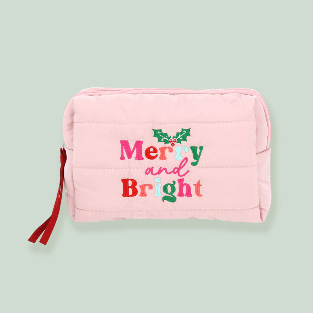 A pink quilted cosmetic pouch bag titled Merry and Bright features festive embroidered lettering in red, green, and pink, along with a decorative holly design.