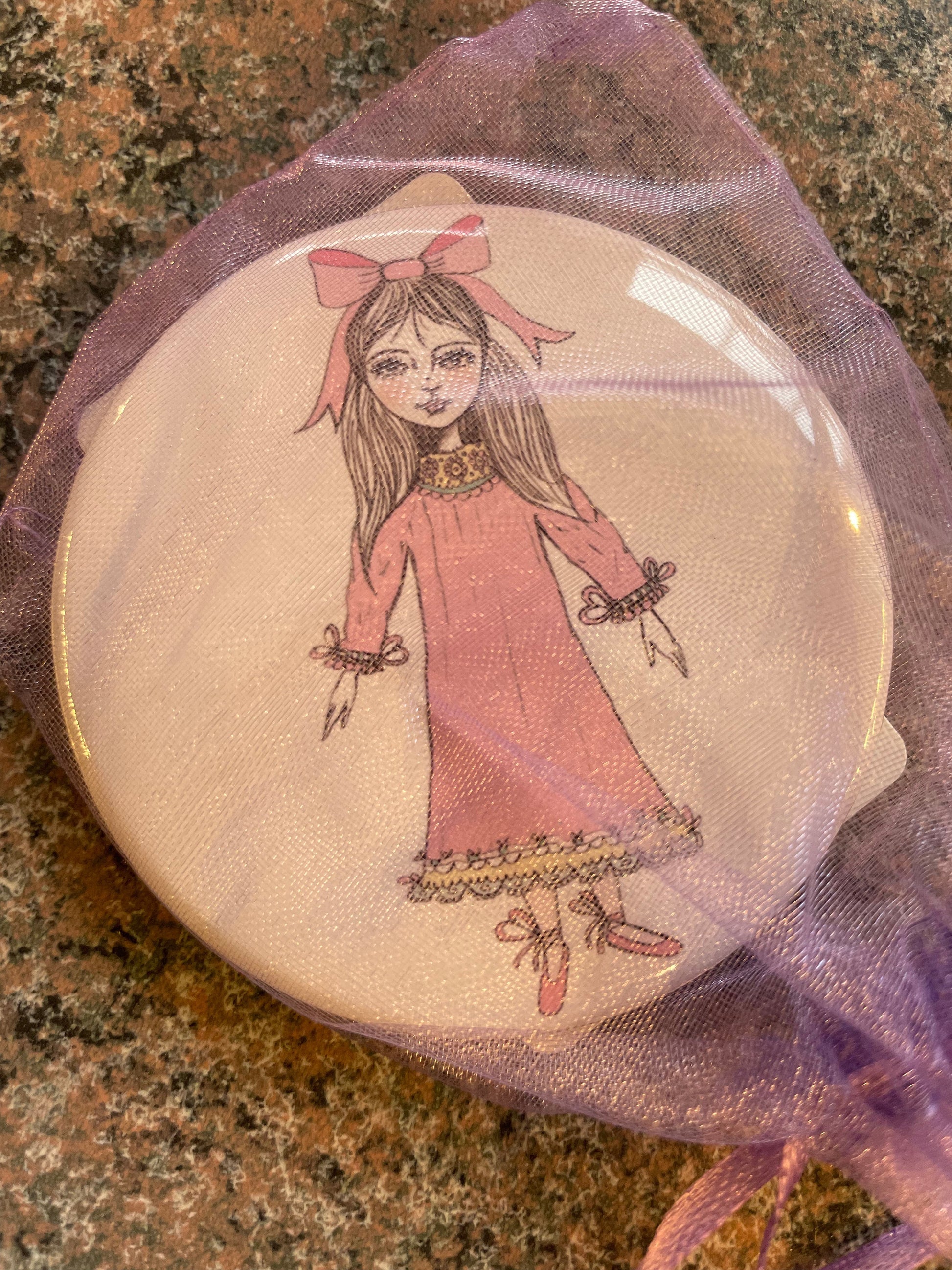 A Nutcracker-themed pocket mirror featuring a whimsical illustration of a girl in a pink dress, adorned with a large bow in her hair.