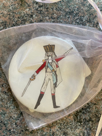 A 3-inch pocket mirror featuring a Nutcracker character in a festive pose, dressed in a red and white uniform with a tall black hat, holding a sword.