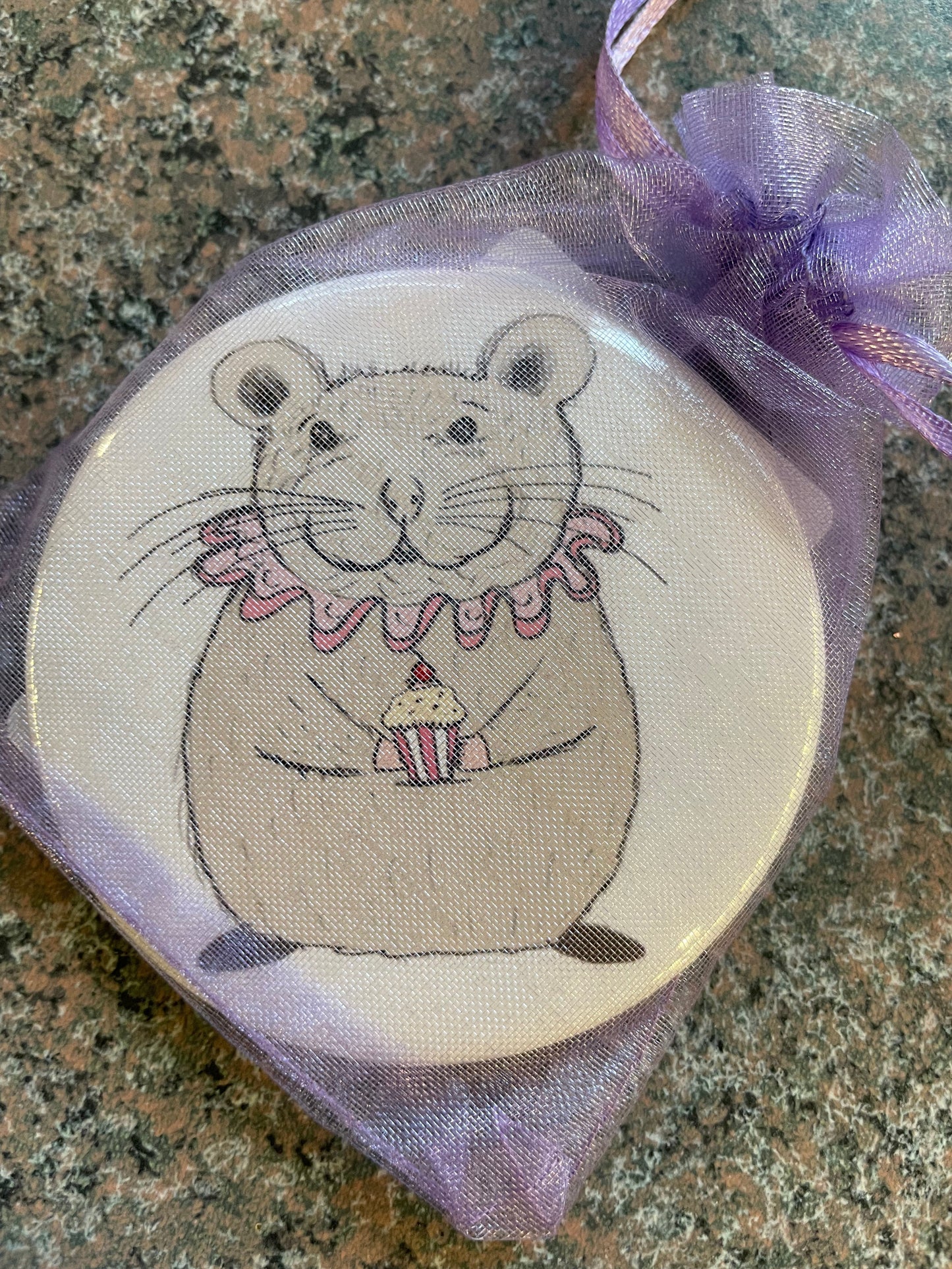A round pocket mirror featuring a cute illustration of a chubby, smiling rodent wearing a pink ruffled collar and holding a small cupcake.