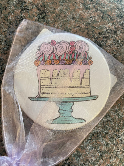 A decorative pocket mirror featuring a whimsical illustration of a cake adorned with pink roses and colorful sprinkles, set on a light blue cake stand.