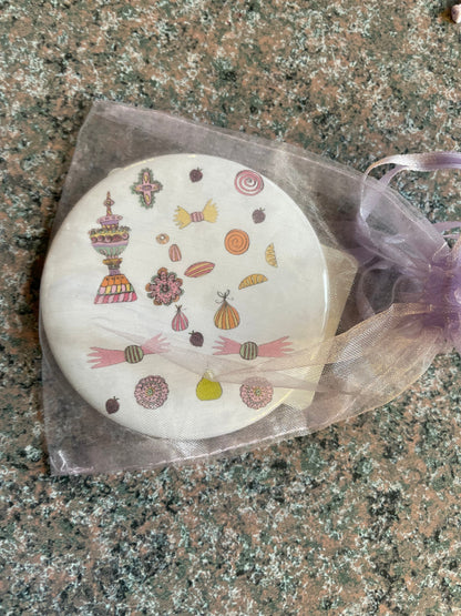 A round, 3-inch pocket mirror featuring festive Nutcracker-themed artwork, adorned with colorful candies and decorative elements.