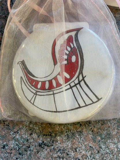 A Nutcracker-themed pocket mirror, featuring a whimsical red and white bird design, is displayed inside a sheer, light-colored drawstring bag.