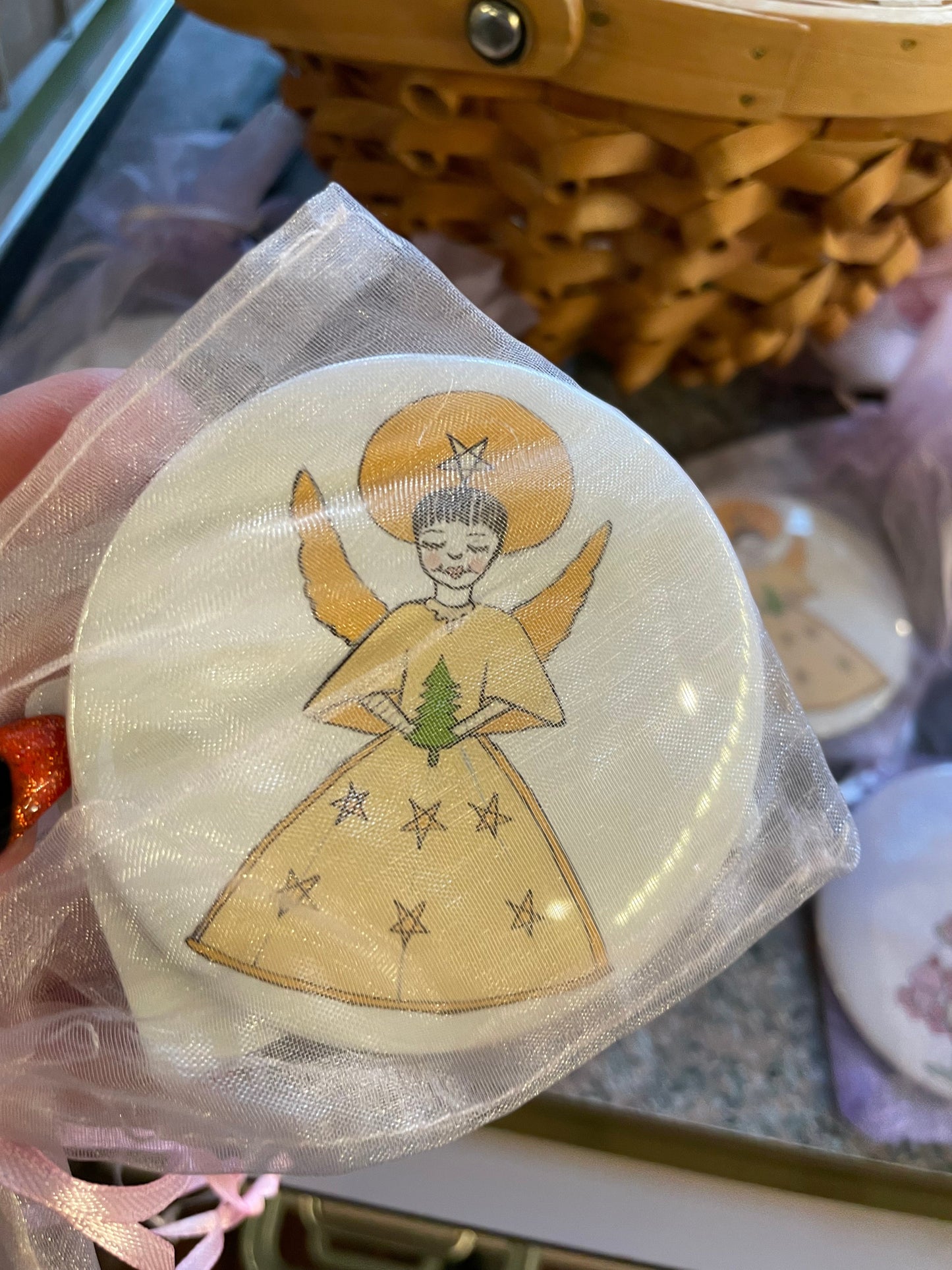 A hand holds a pocket mirror featuring a whimsical angel design, adorned with a golden halo and stars on a cream background.